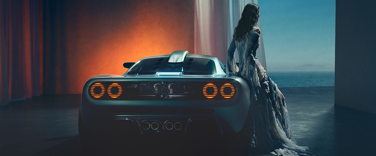 Arrière de la supercar Gordon Murray S1 aux feux allumés avec une femme en robe de soirée au bord de la me