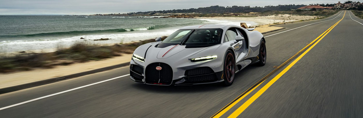 Voiture de luxe Bugatti grise roulant sur une route de bord de mer.