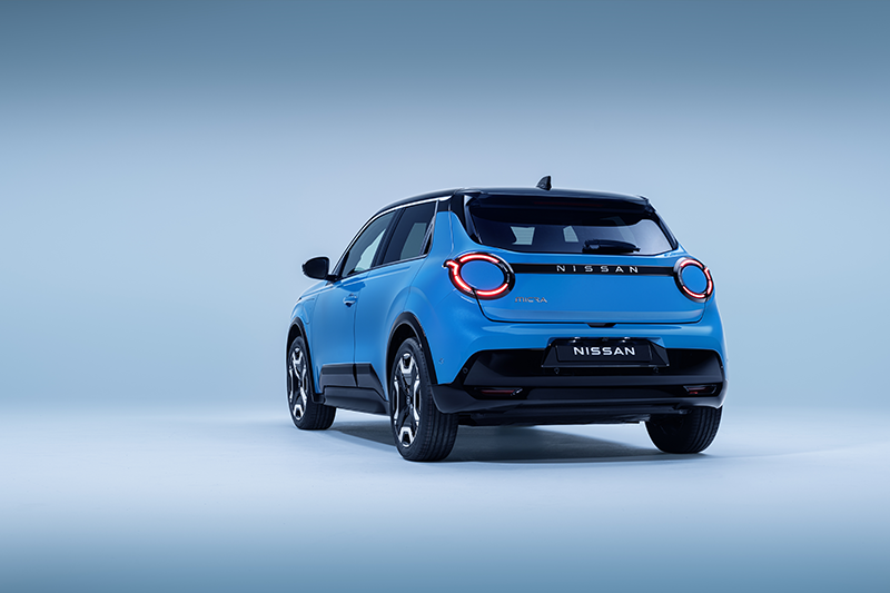 4 view of Micra in blue gear color showing signature lit headlamps. nissan name plate driver passenger doors wheels and black bumper copie