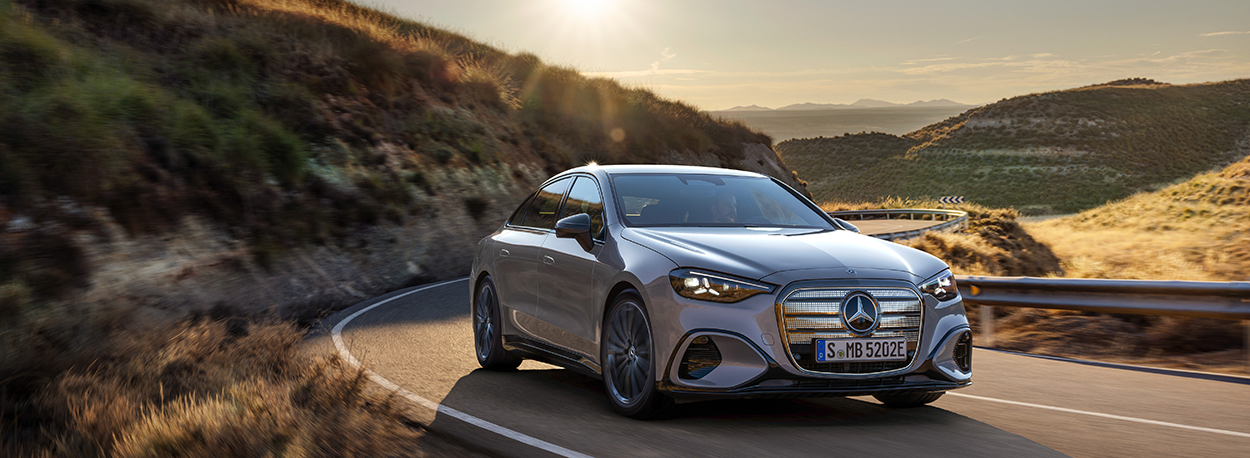 Essai dynamique de la nouvelle Mercedes Classe C électrique 2026 en virage, silhouette de coupé et calandre illuminée sur route de montagne.