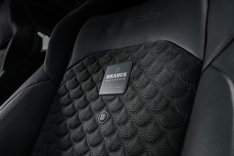 Gros plan sur le dossier d'un siège en cuir noir de la BRABUS BODO, mettant en valeur le matelassage perforé en motif Shell, le badge métallique BRABUS Masterpiece et le logo Double-B.
