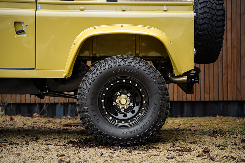 Détail jante noire renforcée et pneu tout-terrain agressif sur Land Rover Defender 90 MIYO Nomad jaune.