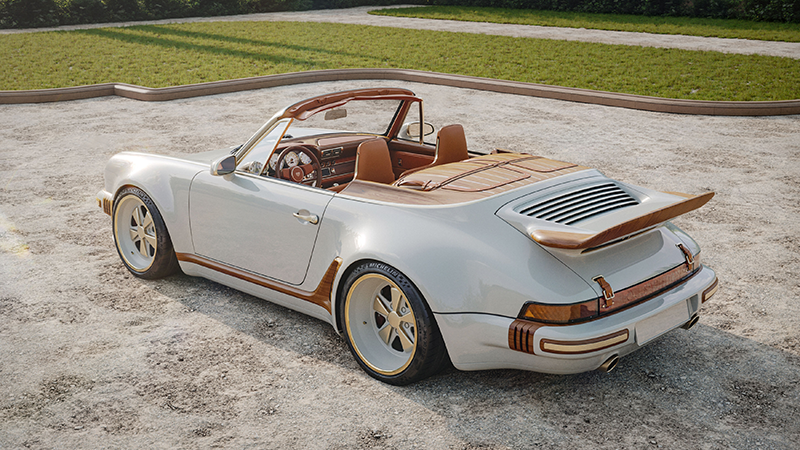 "Vue arrière de trois quarts d'une Porsche 911 Singer Cabriolet blanche avec intérieur en cuir marron et jantes dorées, garée sur une allée de gravier.